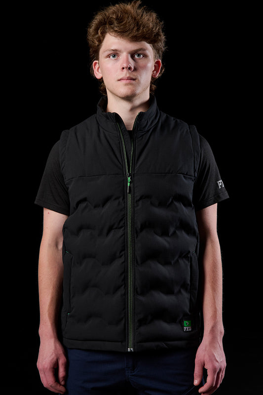 Model wearing FXD WO.6 insulated puffer vest in black with a green front zipper.