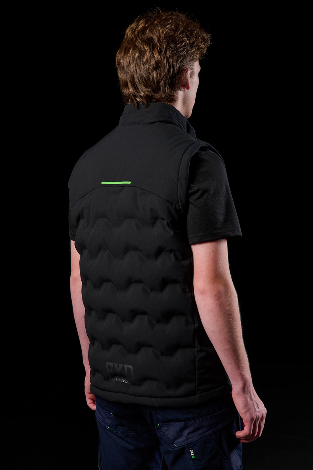 Rear view of FXD WO.6 insulated puffer vest on a model, featuring a lime green reflective stripe on the back.