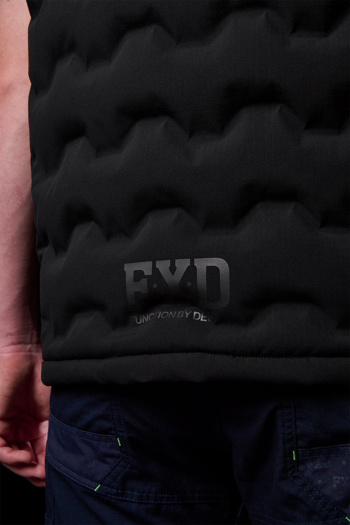 Close up of the lower back area of the FXD WO.6 vest showing quilted black fabric and EXD branding.