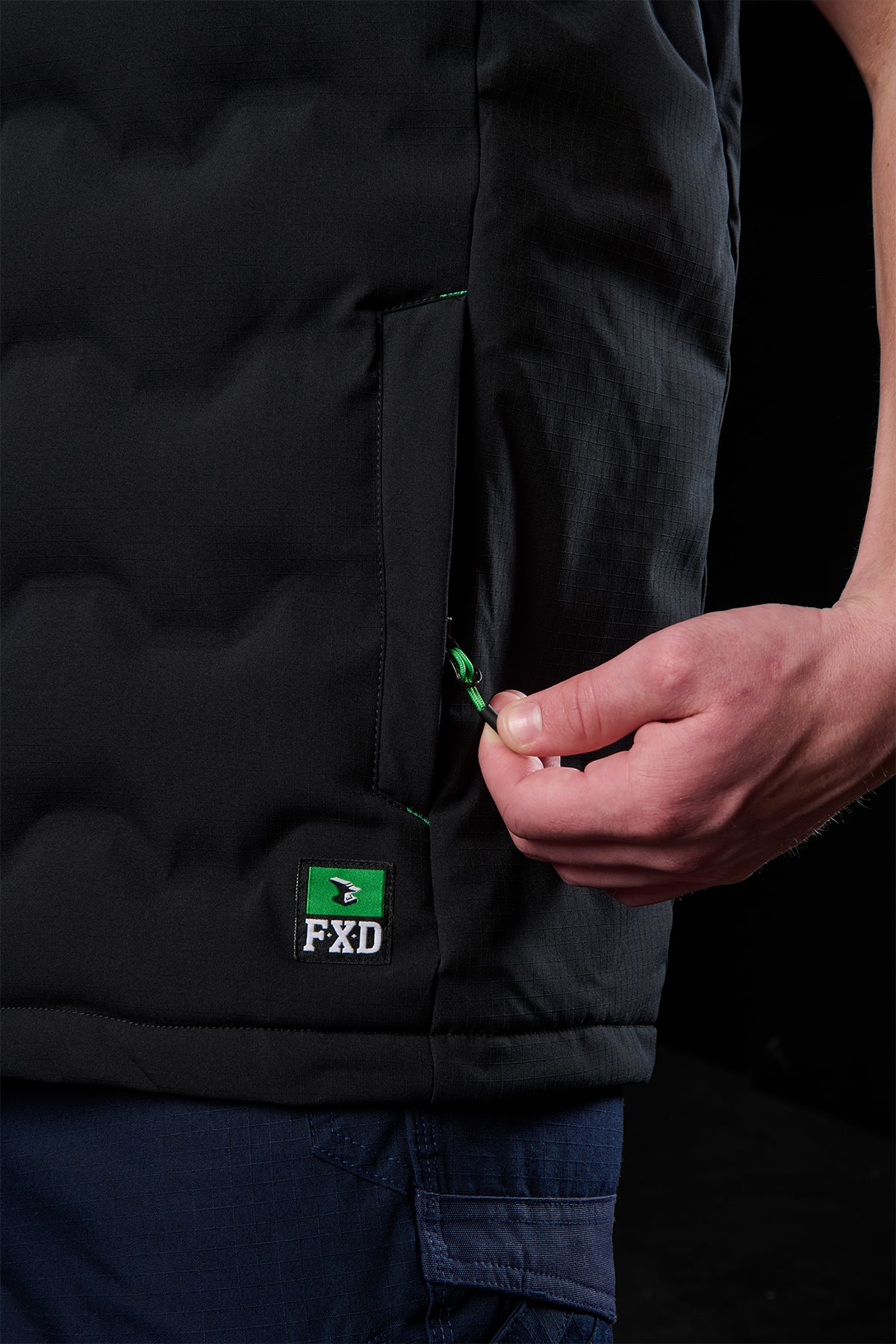 Side view of black FXD WO-6 vest showing a zip pocket and green zipper pull