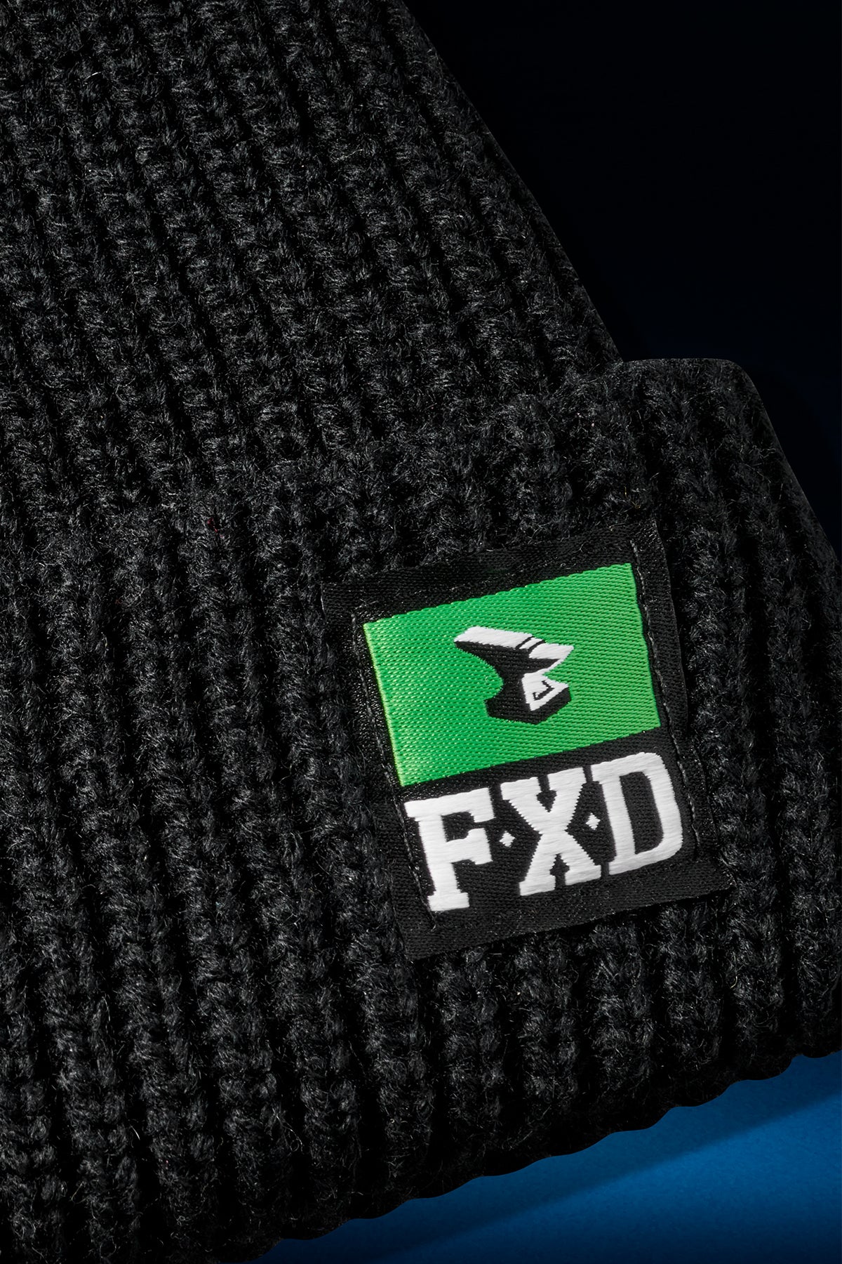 Close up of black knit beanie featuring a green FXD label stitched to the edge